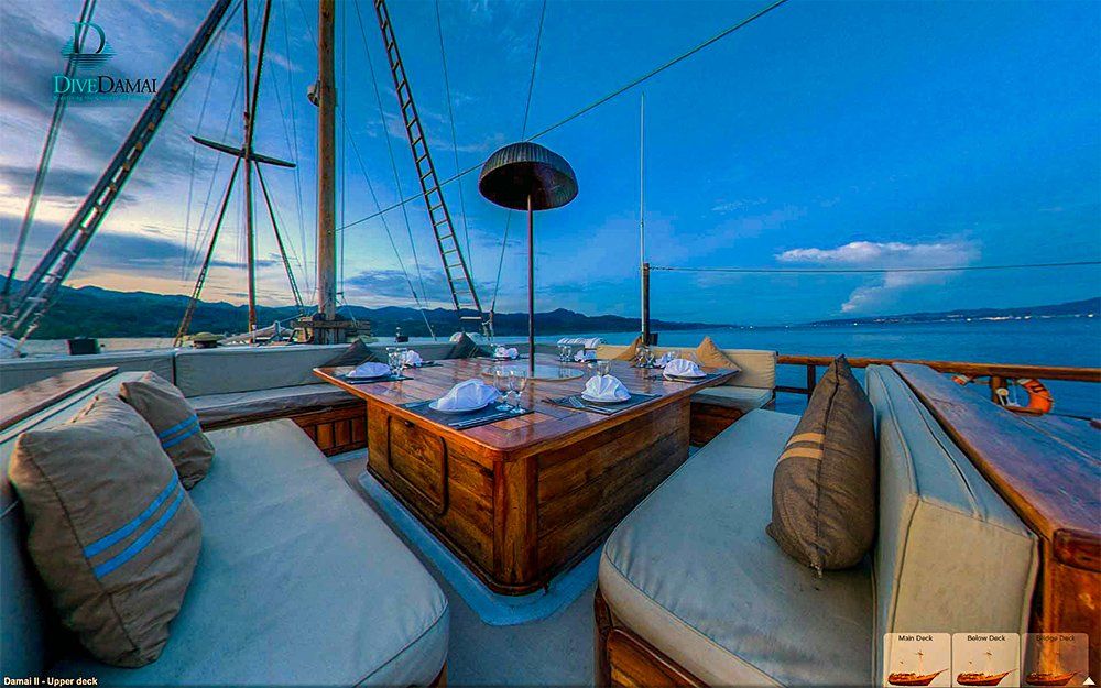 Wooden yacht deck at dusk, with dining table set and cushioned seating, overlooking a calm sea.