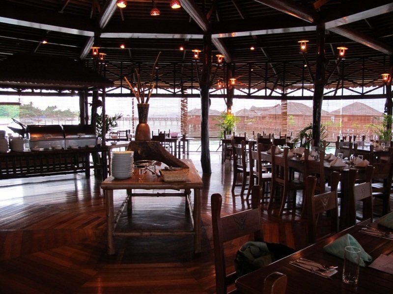 Restaurant interior with wooden tables and chairs, buffet, and water view.