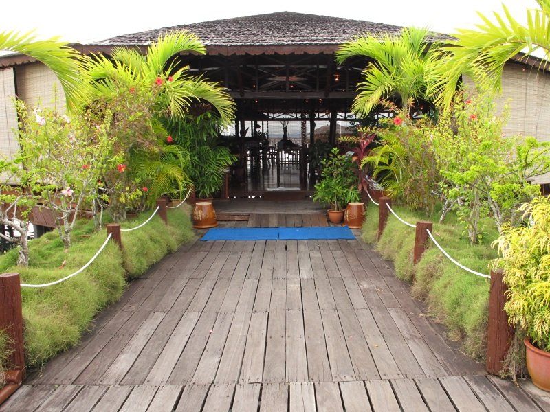 Wooden walkway leading to a tropical restaurant with lush greenery.