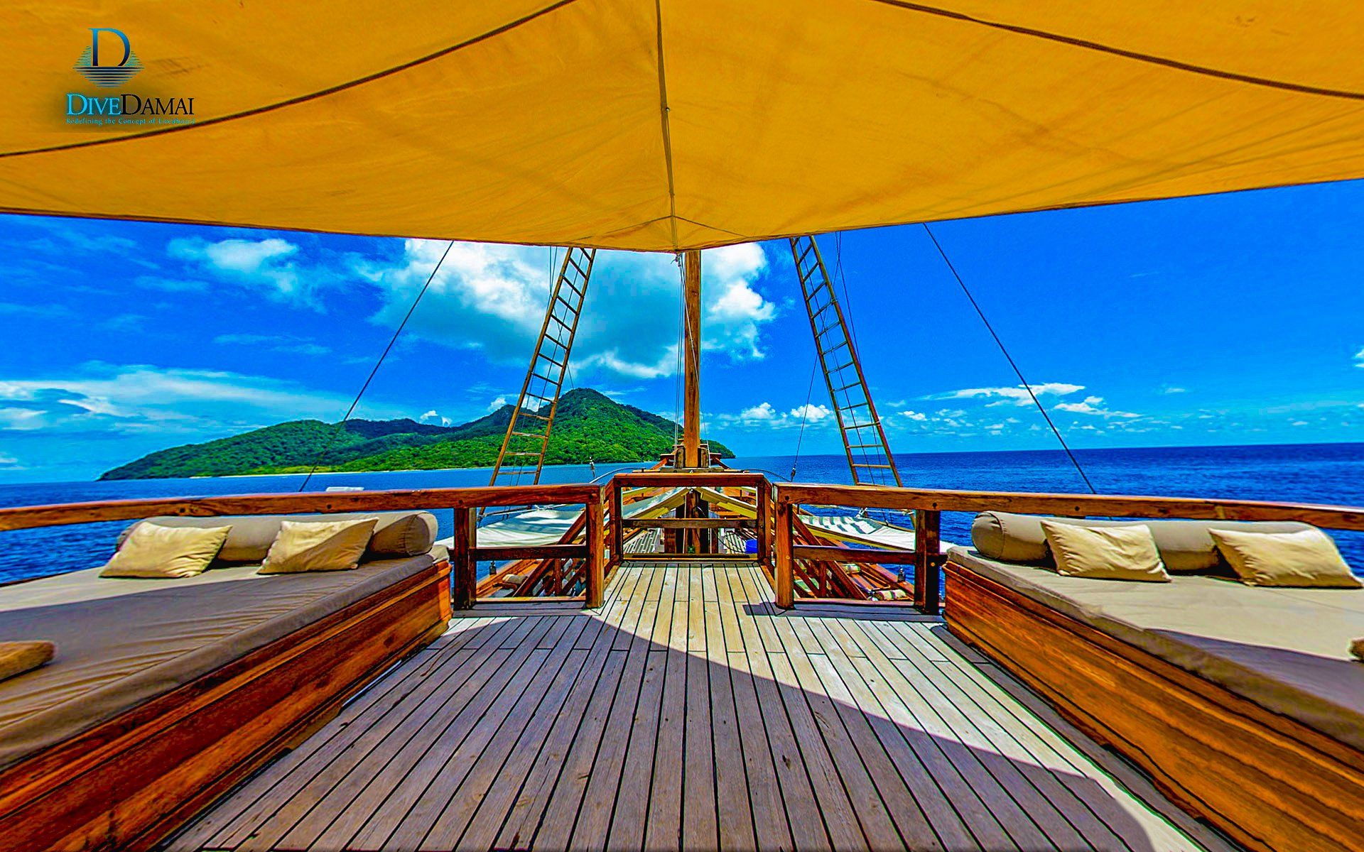View from a boat with sunbeds, awning, towards tropical island, blue sea, sky.