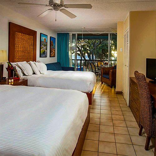 Hotel room with two queen beds, desk, and balcony overlooking trees.