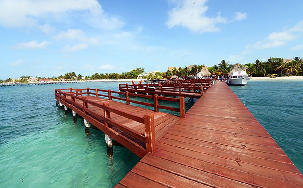 Wooden pier extending into clear turquoise water with a boat docked on the right and buildings in the background under a blue sky.