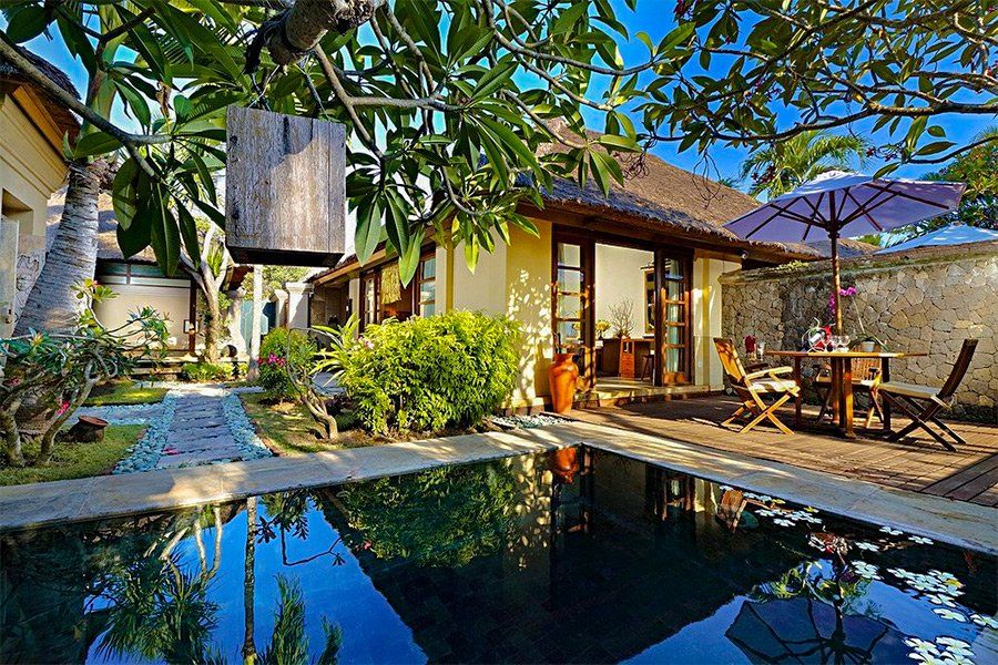 Tropical villa with pool, outdoor dining, and thatched roof under a sunny blue sky.