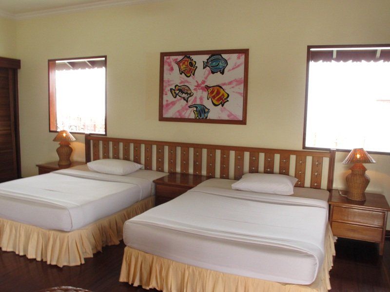 Two beds with white bedding, wooden headboard, bedside tables, and a framed art piece in a room with two windows.