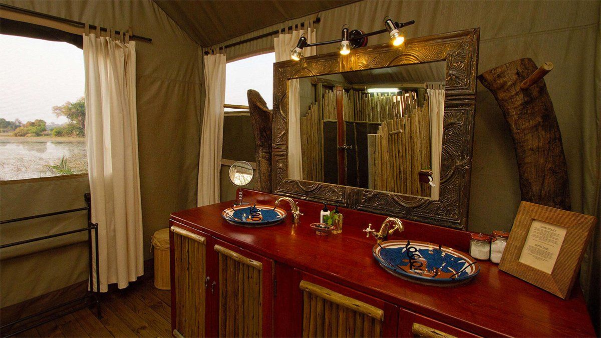 Bathroom in a tent with red vanity, ornate mirror, and window overlooking a body of water.
