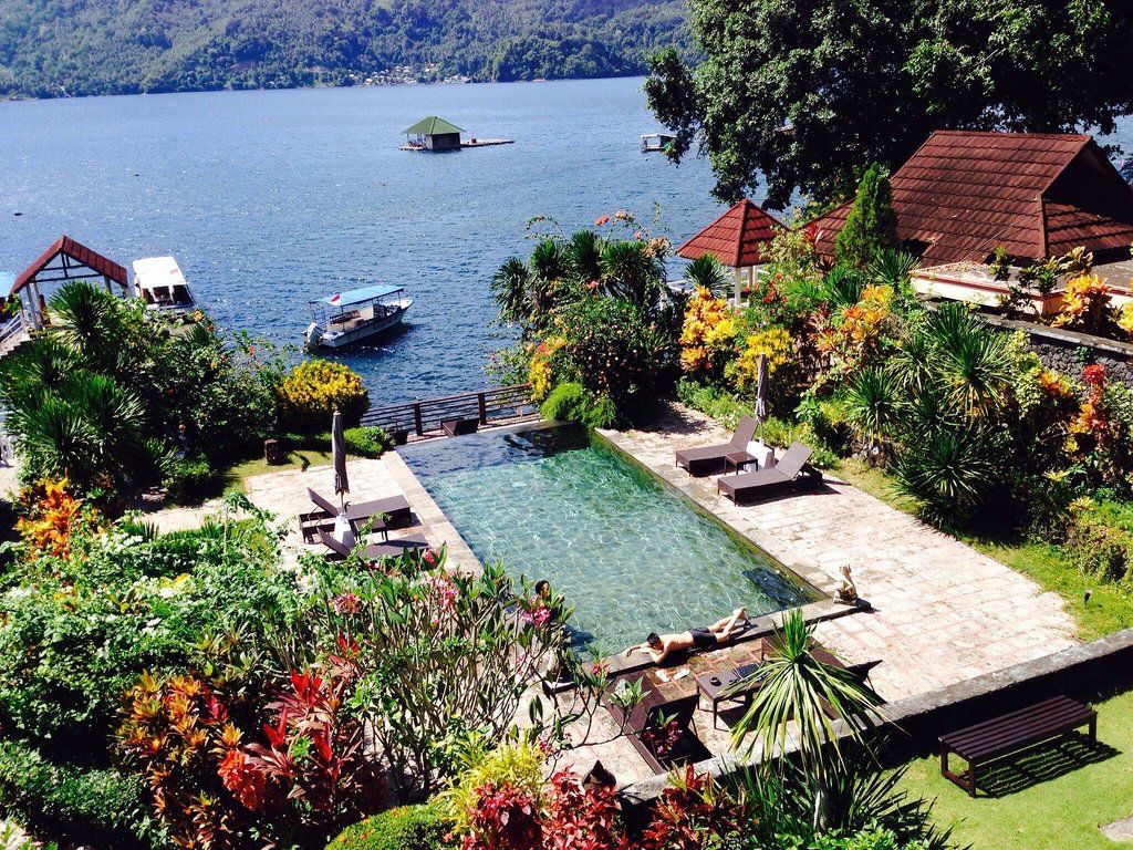 Pool overlooking a lake with boats, surrounded by lush greenery and buildings with red roofs.