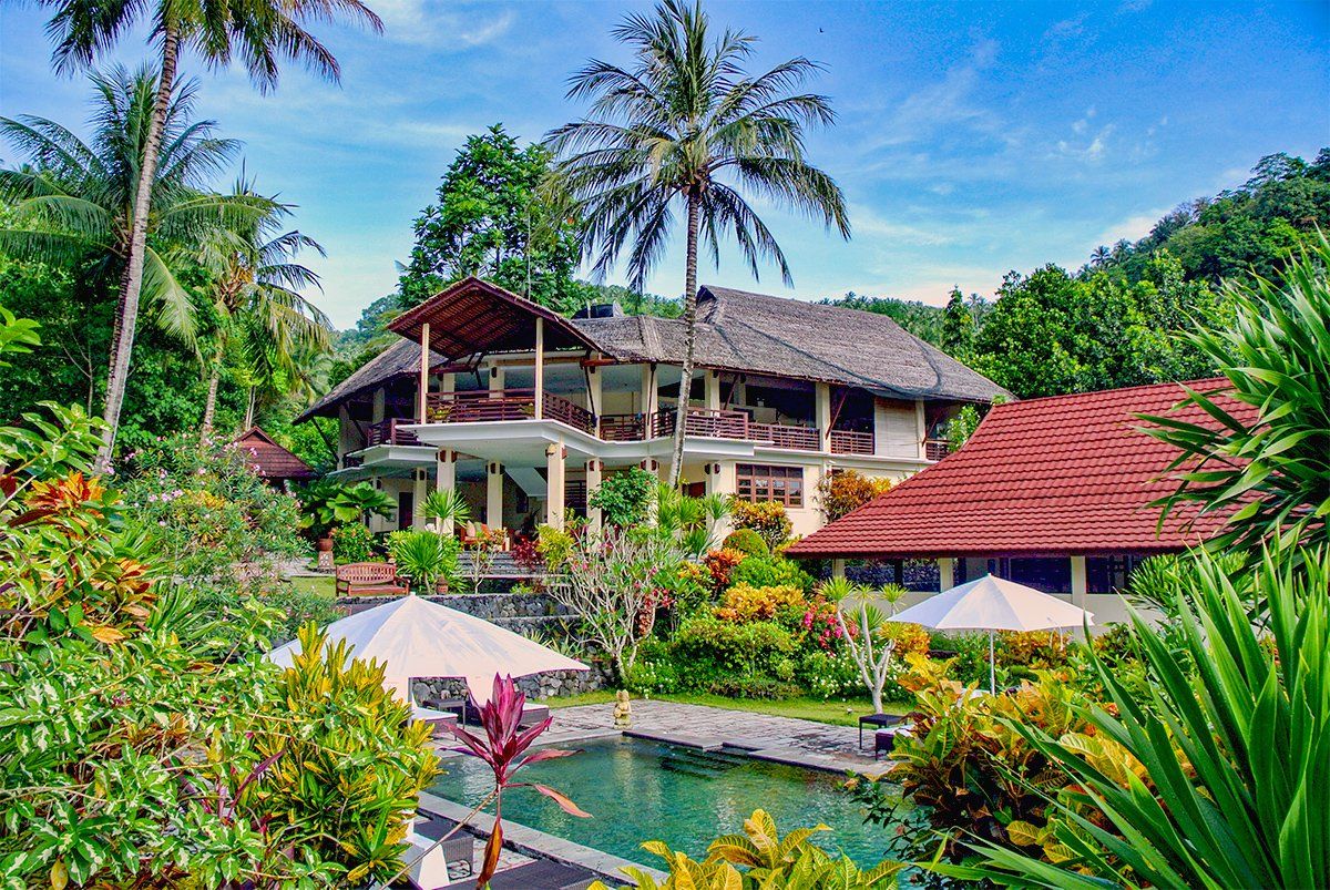 Tropical resort with a pool, palm trees, and multi-story buildings with a red-tiled roof.