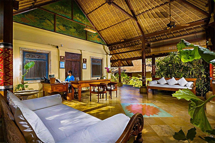 Hotel reception area with a person at the desk, open-air seating, and a thatched roof.