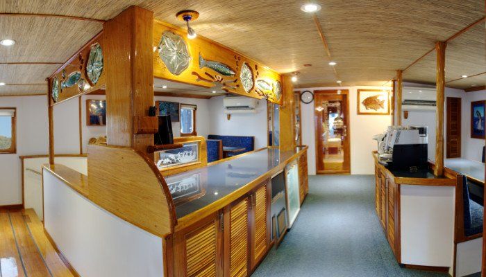 Interior of a boat with wooden bar, counter and cabinets. Decorative fish art on the wall.
