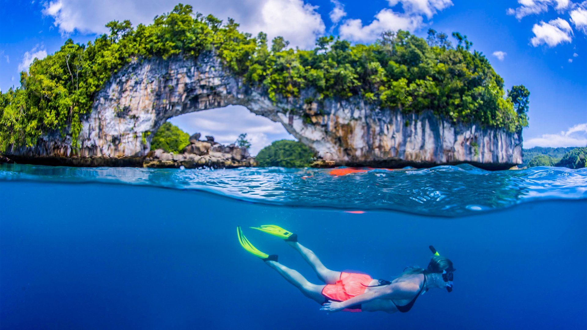 Person snorkeling in turquoise water near a rock island with a natural arch.