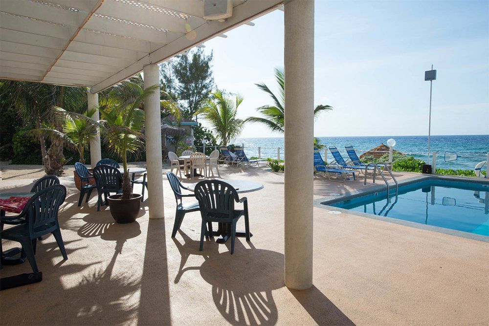 Patio overlooking ocean, chairs and pool under awning, sunny day.