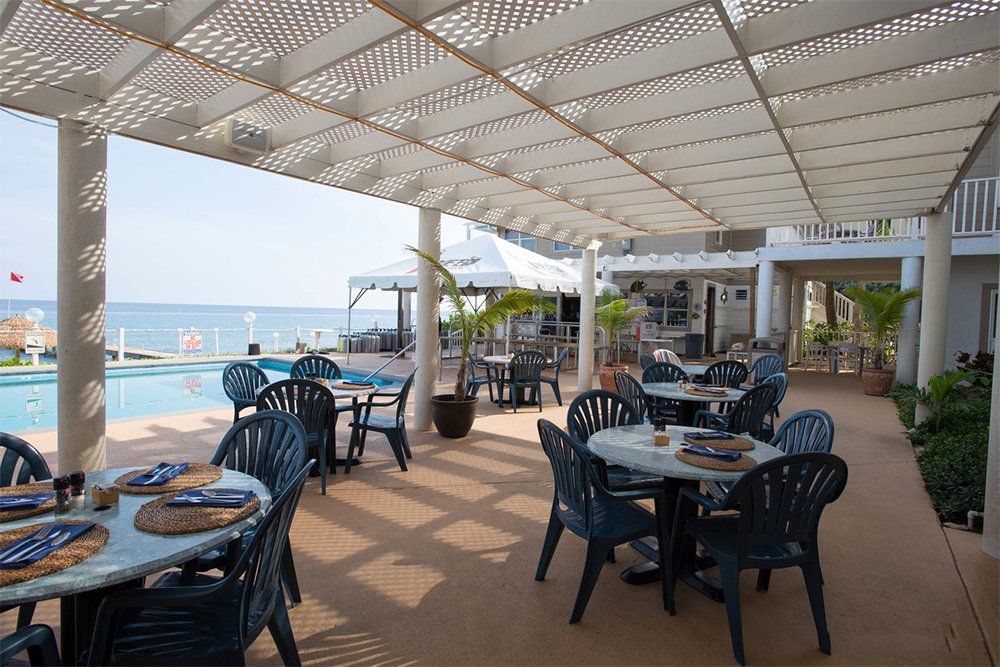 Outdoor restaurant patio with tables, chairs, and view of pool and ocean.