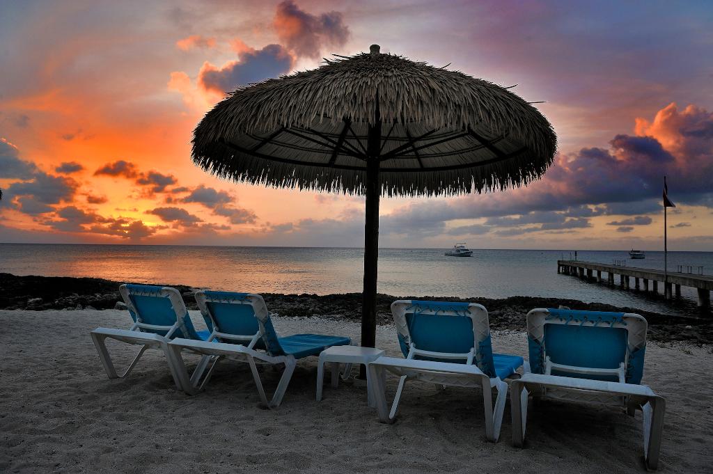 Beach chairs under a thatched umbrella at sunset, looking out at the ocean.