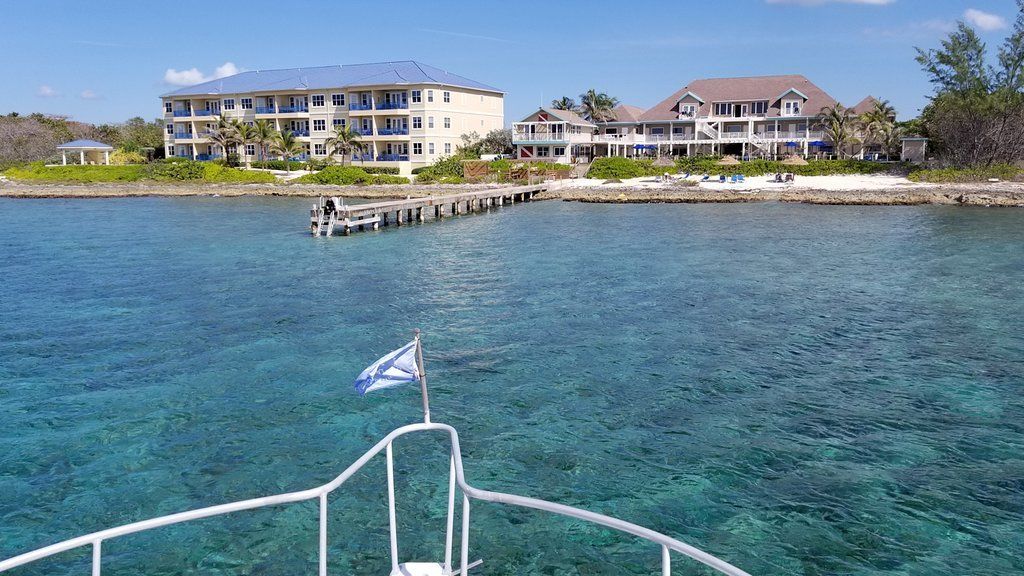 Boat approaching a pier with buildings on a coastline, clear blue water, sunny day.