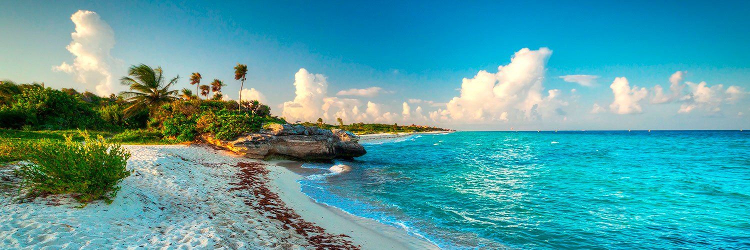 Turquoise ocean meets white sand beach under a bright blue sky with puffy white clouds.