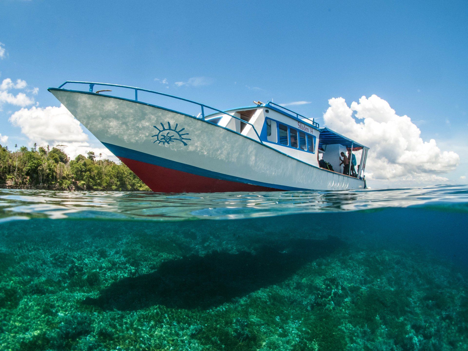 Boat floating over clear, shallow water. Blue sky, white boat with red trim, underwater view.
