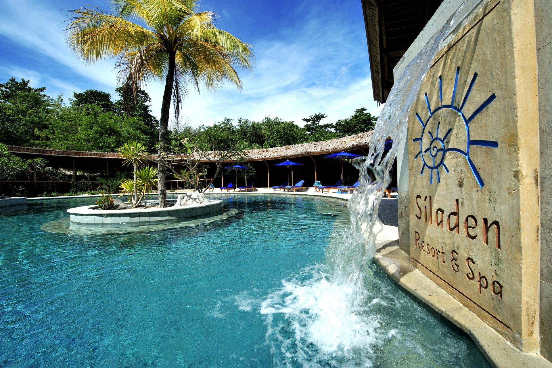 Pool at Siladen Resort & Spa with waterfall feature and blue sky.