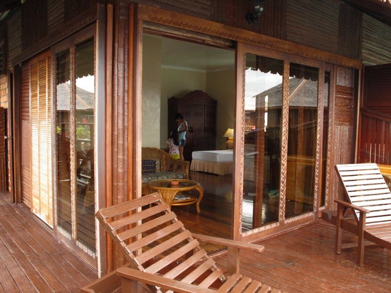 Wooden patio with lounge chairs, open sliding glass doors leading to an interior with furniture, and a person.