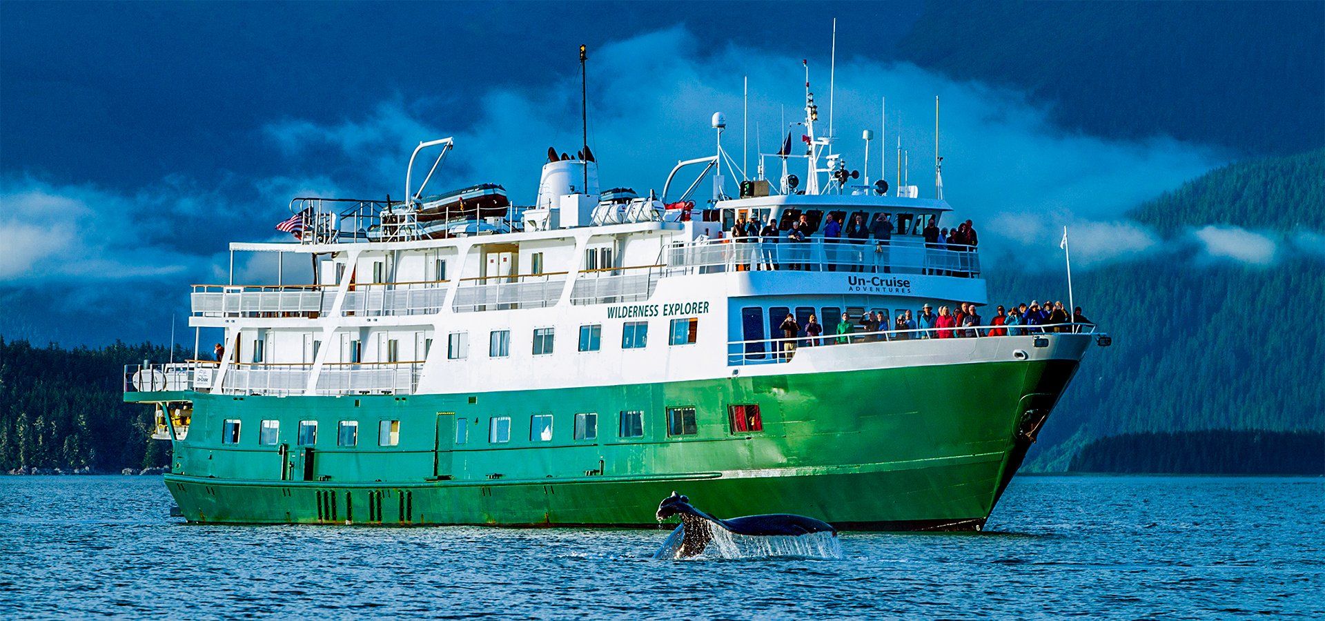 A green and white ferry boat on the water near mountains.