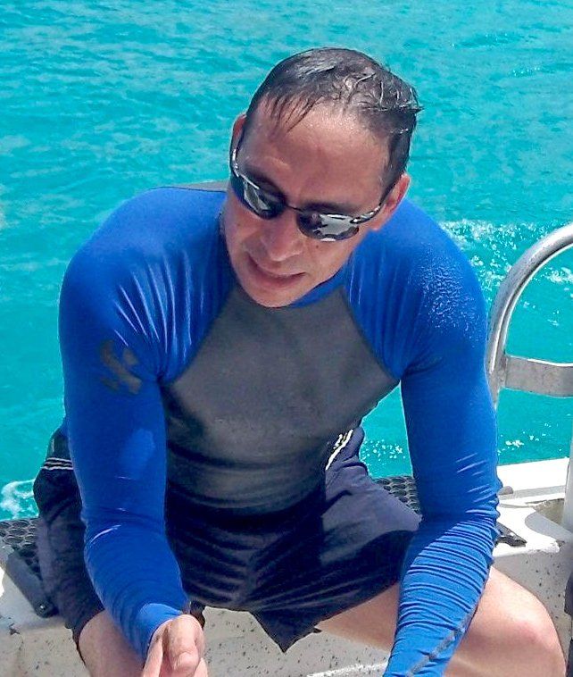 Man in blue long-sleeved shirt and sunglasses on a boat, looking down at the water.