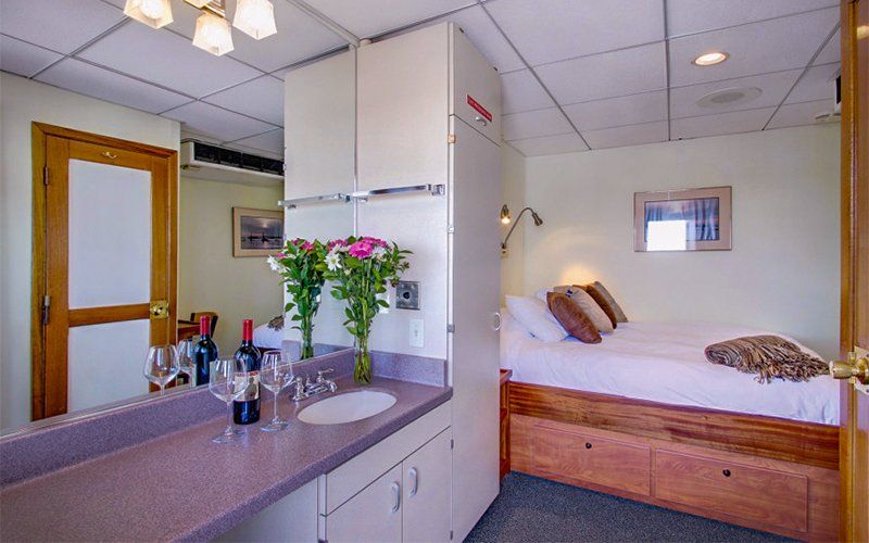 Small hotel room with double bed, sink, and storage. Flowers, wine, and lighting visible.