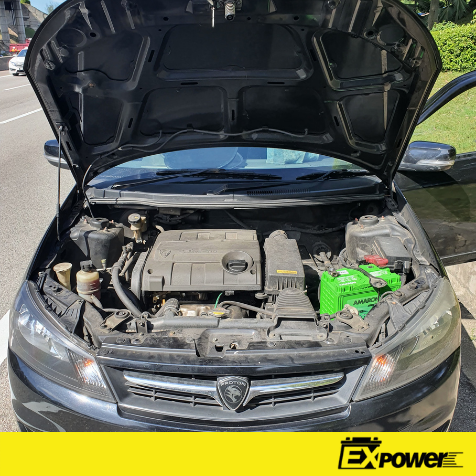 Car engine bay with hood open, showing a green battery and exposed components under the hood.