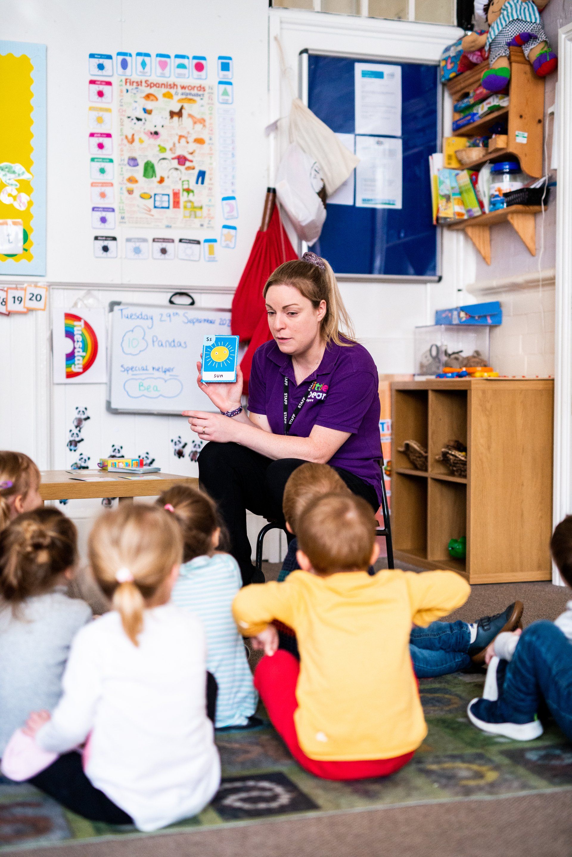 Teacher in purple shirt teaching a group of children in a classroom.