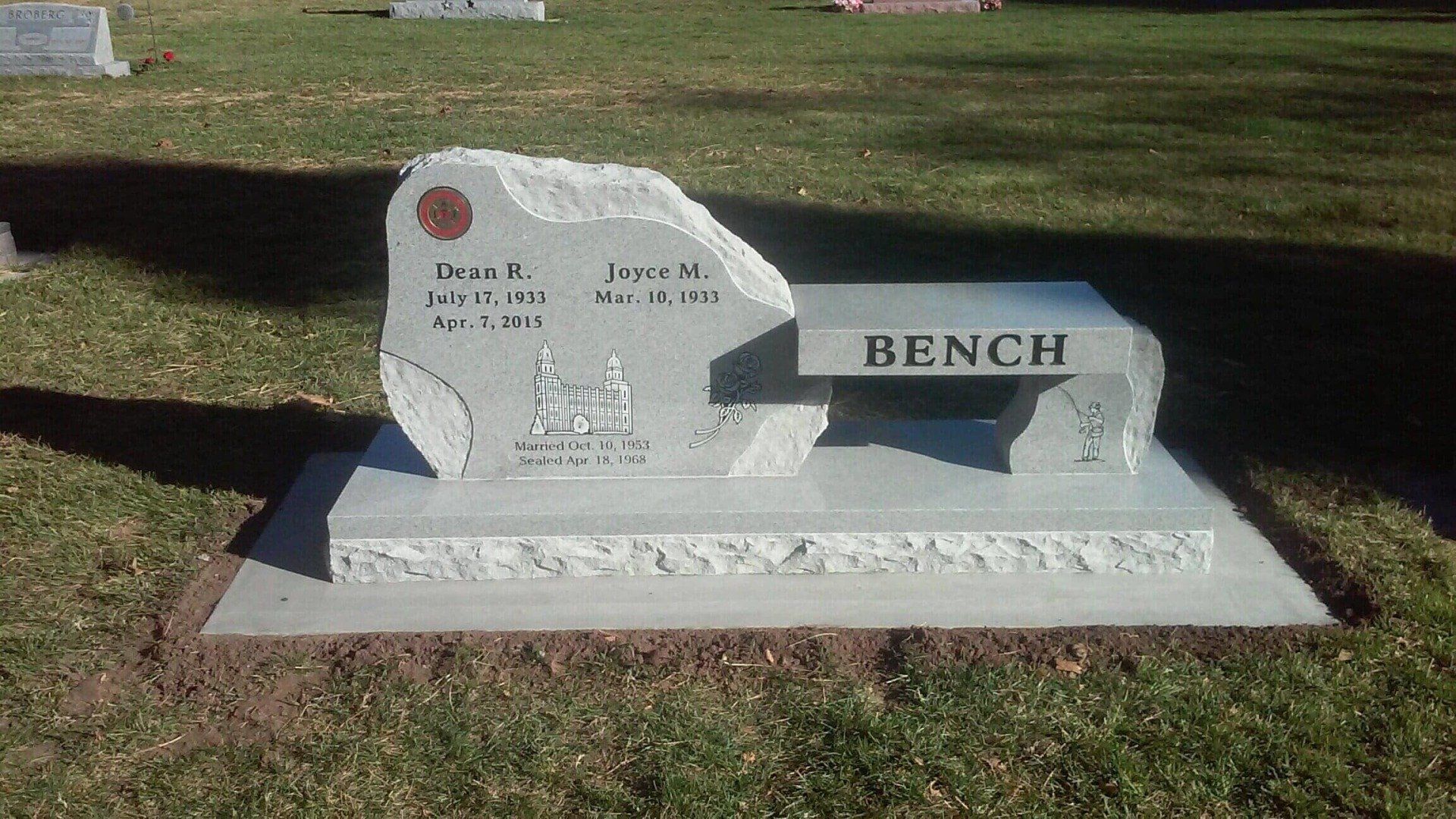 Gravestone shaped like a bench, with names and dates. Located outdoors.