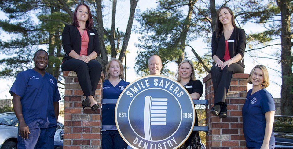 Smile Savers Dentistry staff posing by their sign, some sitting on a brick wall.