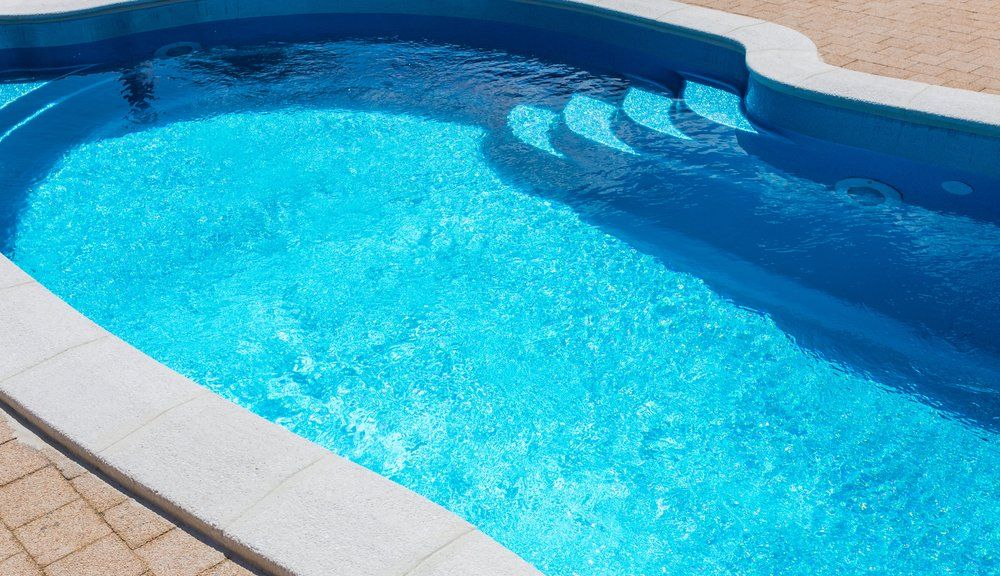 Swimming pool filled with clear blue water, steps, and white tile border.