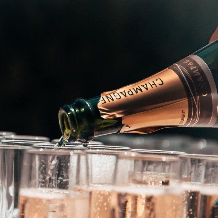 Champagne being poured from a bottle into a row of glasses.