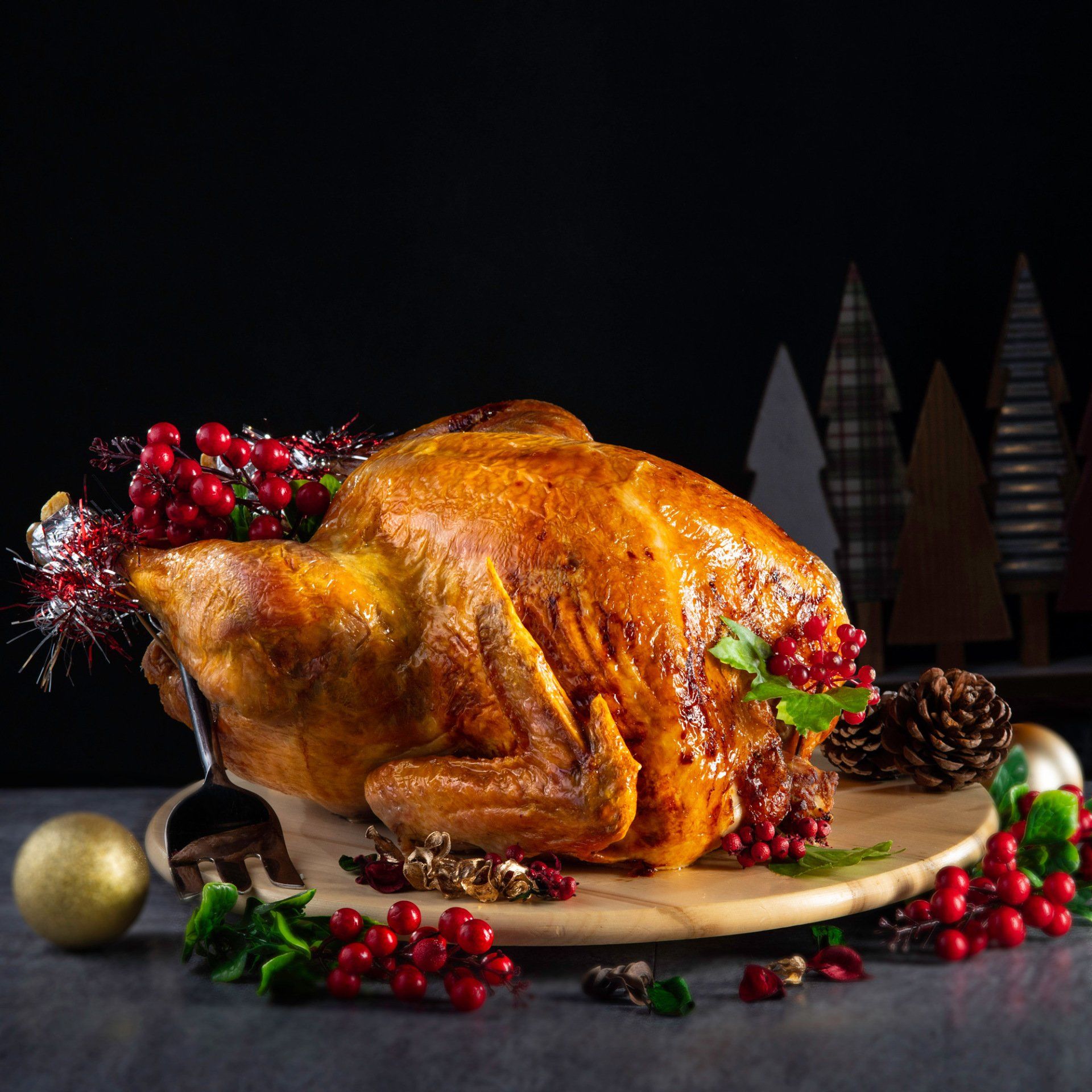Roasted turkey garnished with berries on a wooden board; holiday decorations in background.
