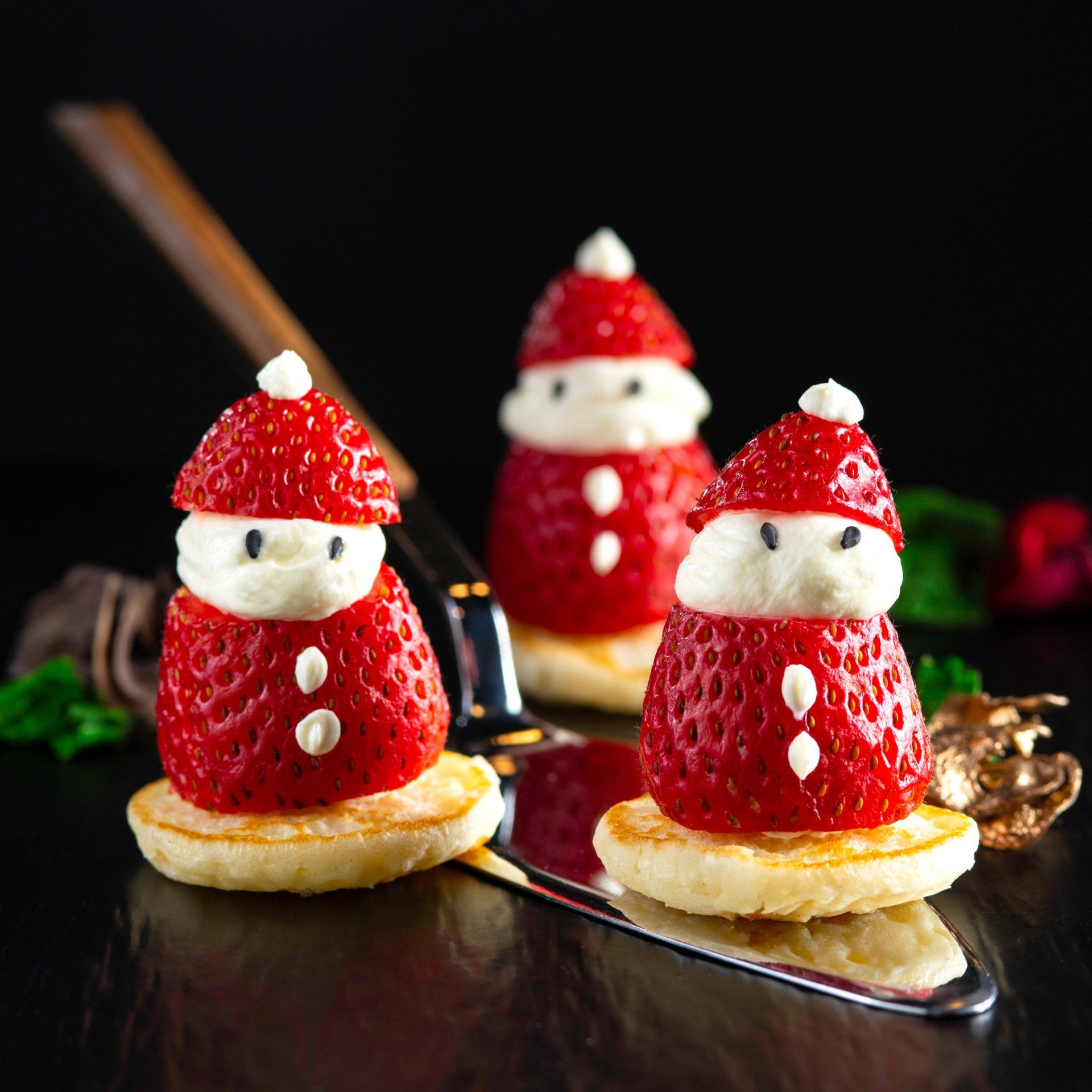 Strawberry Santa Claus figures with whipped cream faces and button details atop small pancakes.