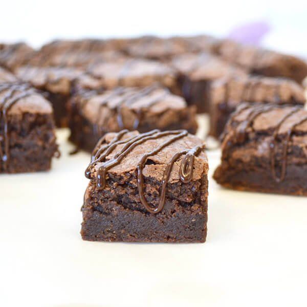 Brownie squares drizzled with chocolate on a white surface.