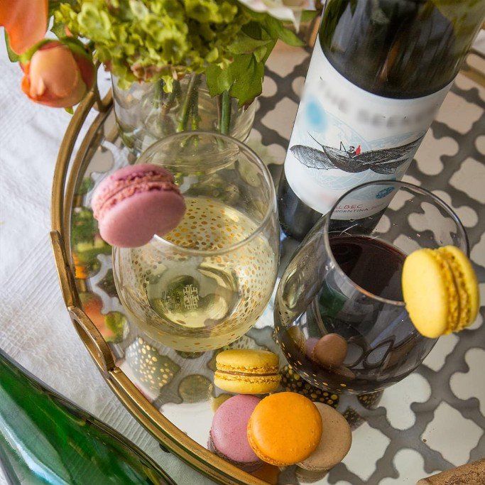 A tray with wine glasses, macarons, wine bottle, and flowers. Yellow and pink macarons accent the tray.