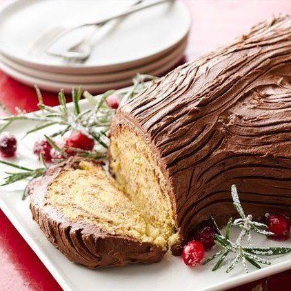 Chocolate Yule log cake with slice cut, on white platter with cranberries and rosemary.