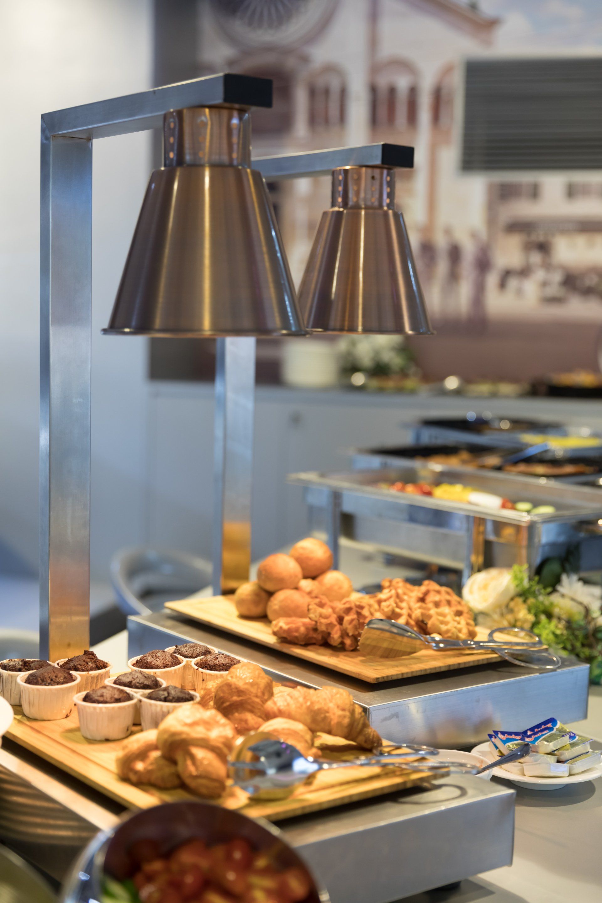 Food buffet with warming lamps; pastries, rolls, and other dishes on display.
