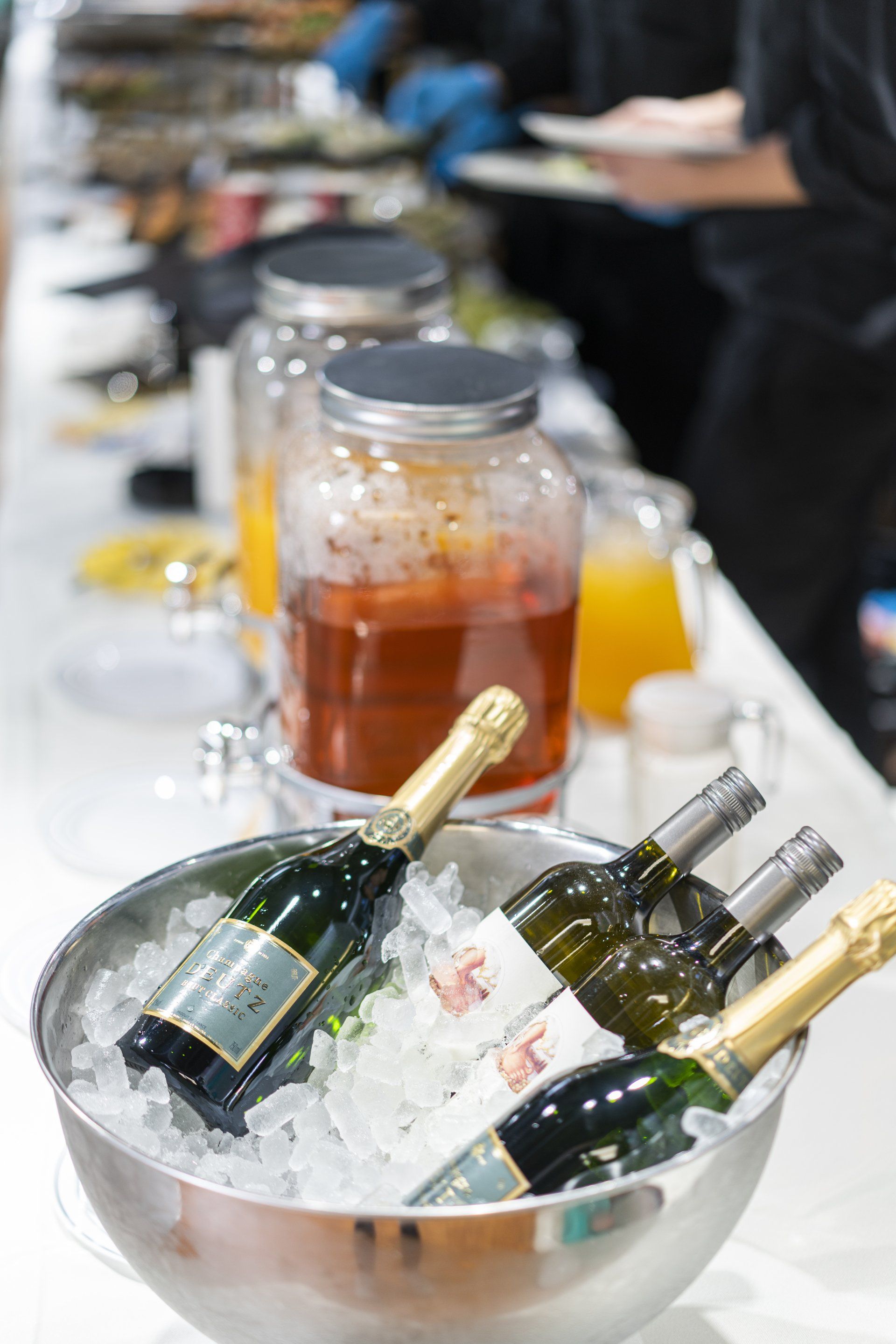 Champagne and white wine bottles in ice bucket, drinks in jars on a buffet table.