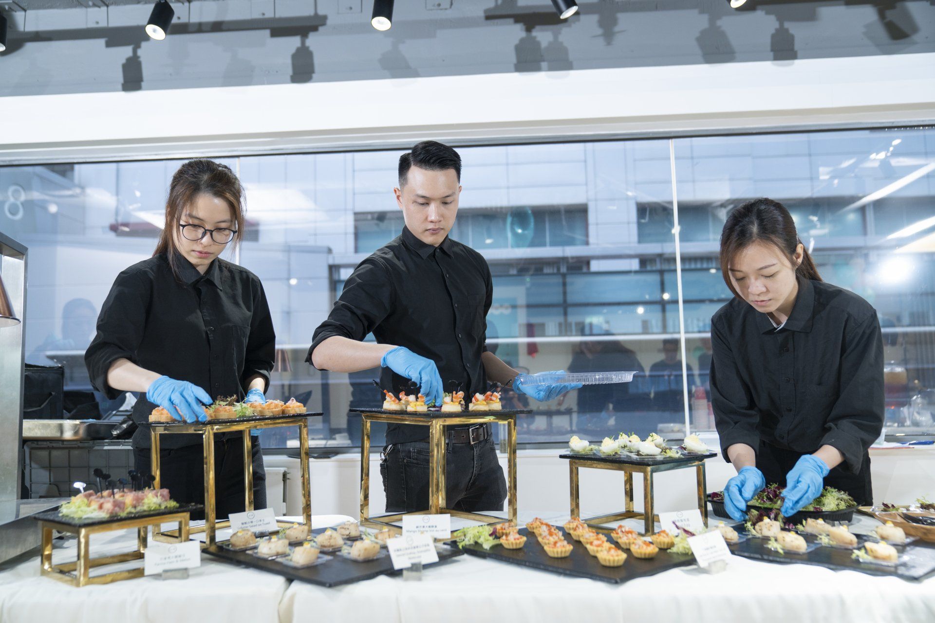 Three people in black shirts and gloves arranging hors d'oeuvres at an event.