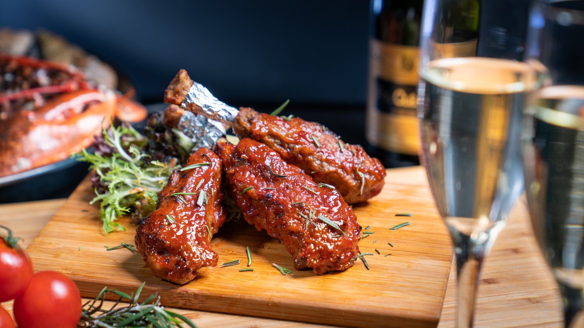 Chicken wings with rosemary on a wooden board, with champagne flutes and tomatoes.