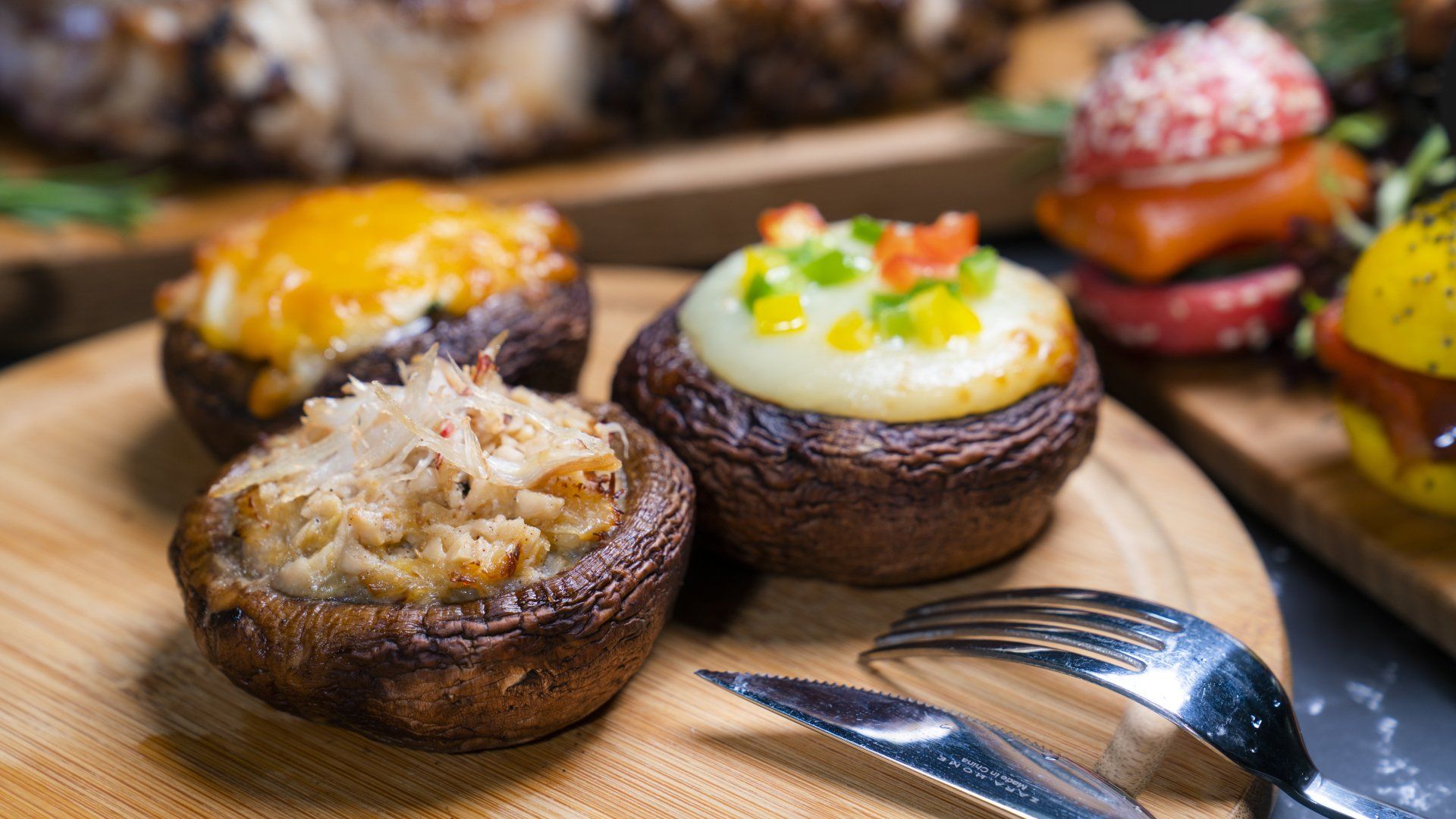 Stuffed mushrooms on a wooden board, with various toppings. Silverware in the foreground.