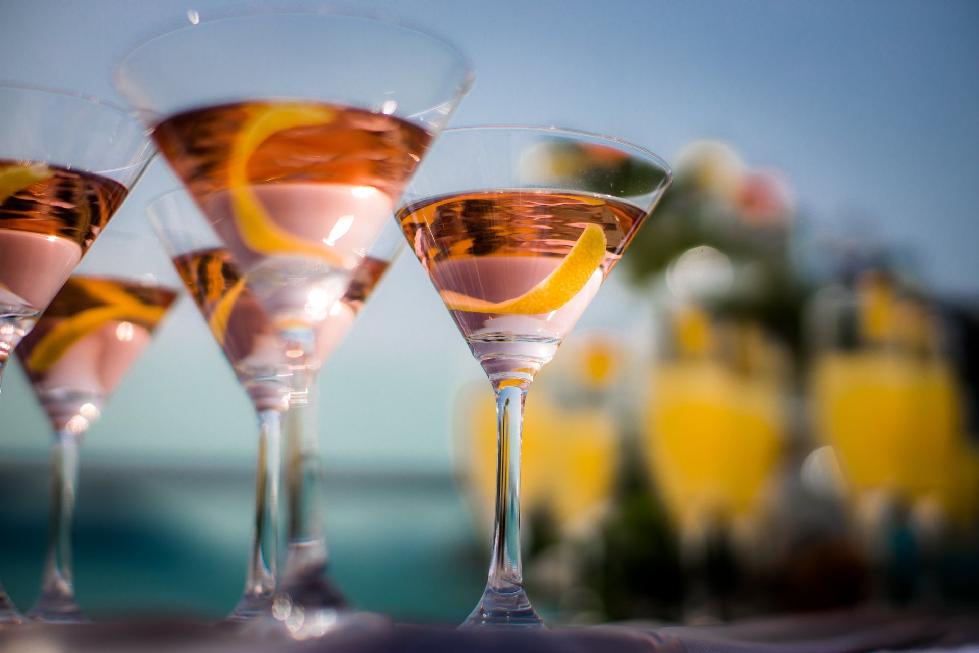Martini glasses with pink cocktails and lemon twist garnishes, outdoors.
