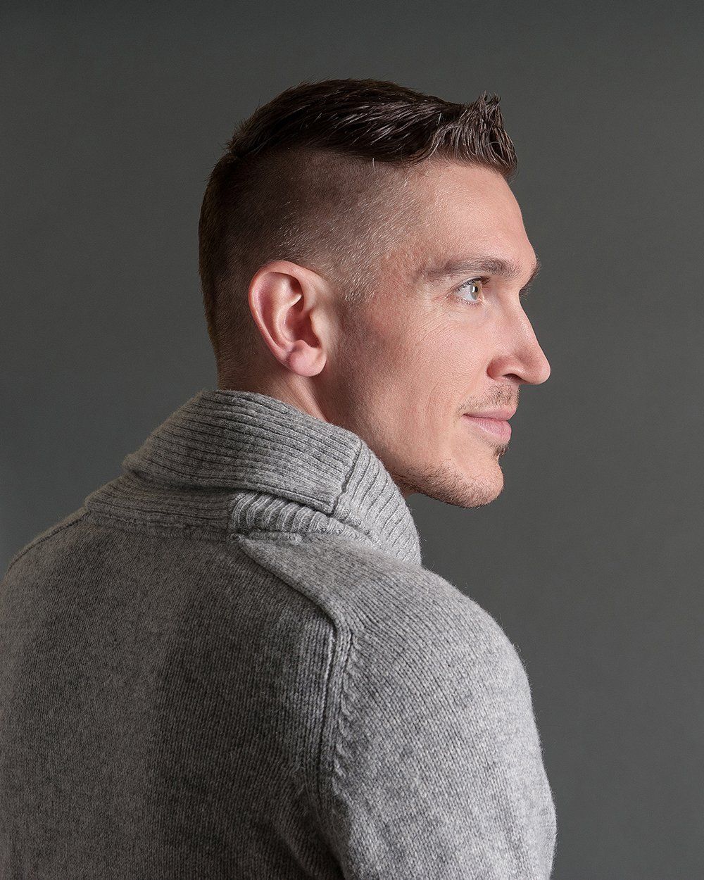 Ein Mann in einem grauen Pullover schaut über seine Schulter.