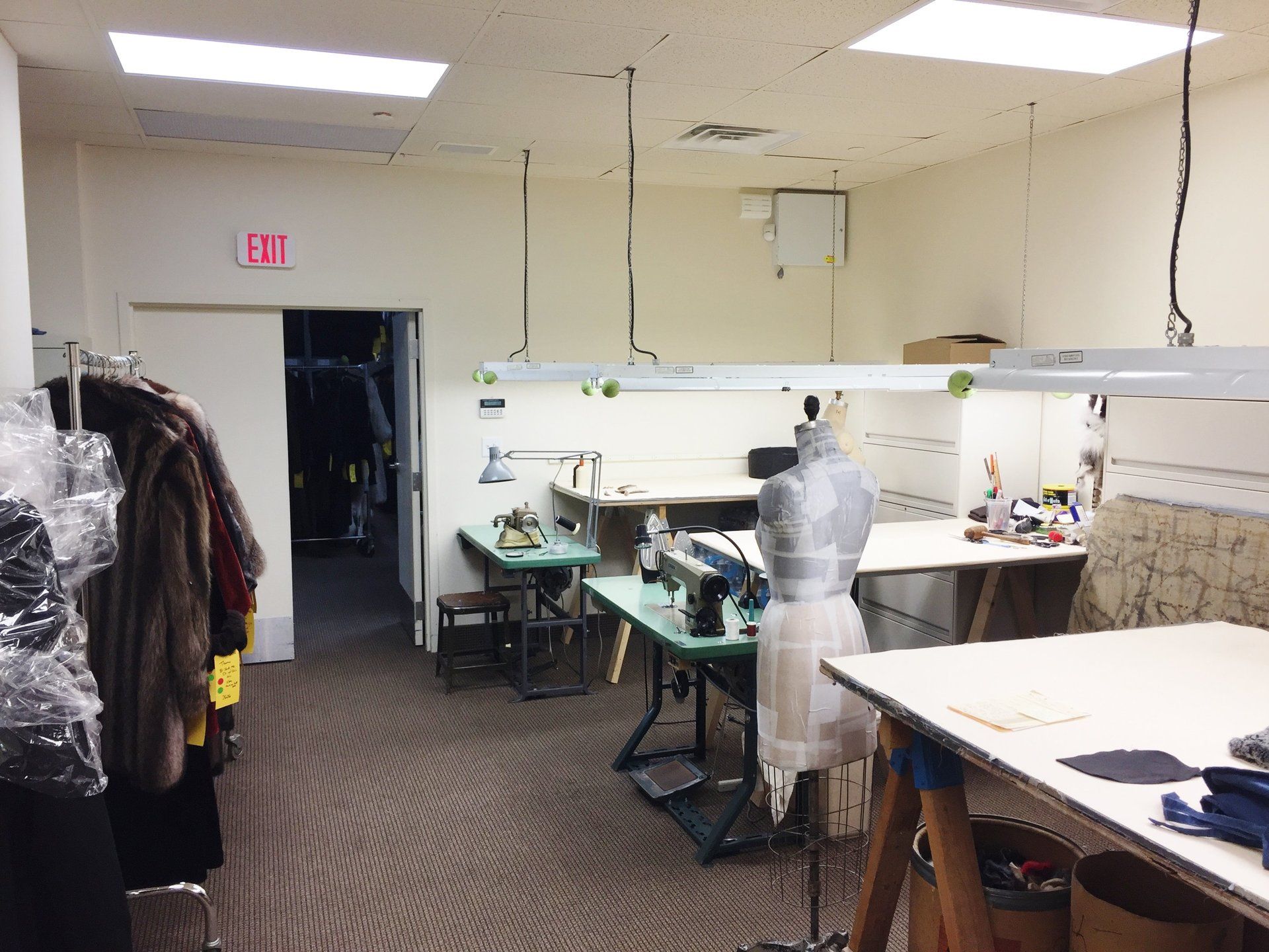 A sewing room with a red exit sign on the wall.