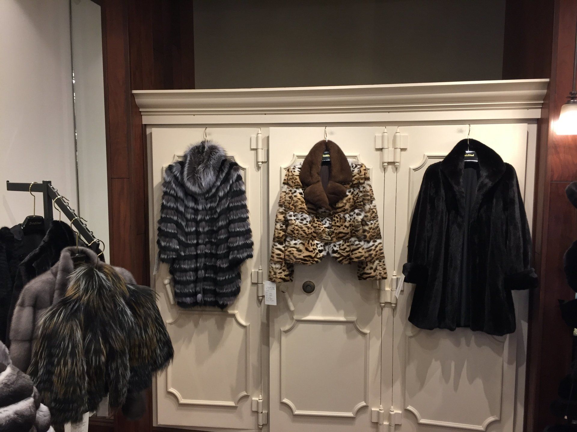 Three fur coats are hanging on a wall in a store
