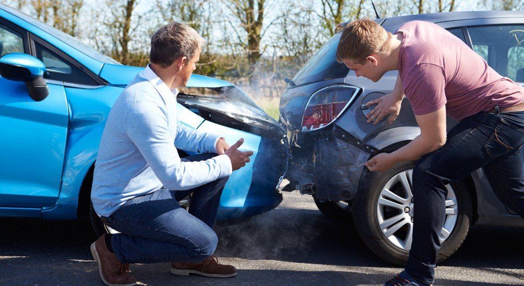 two men are looking at a car that has been involved in a car accident .