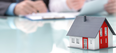 a model house is sitting on a table next to a person signing a document .