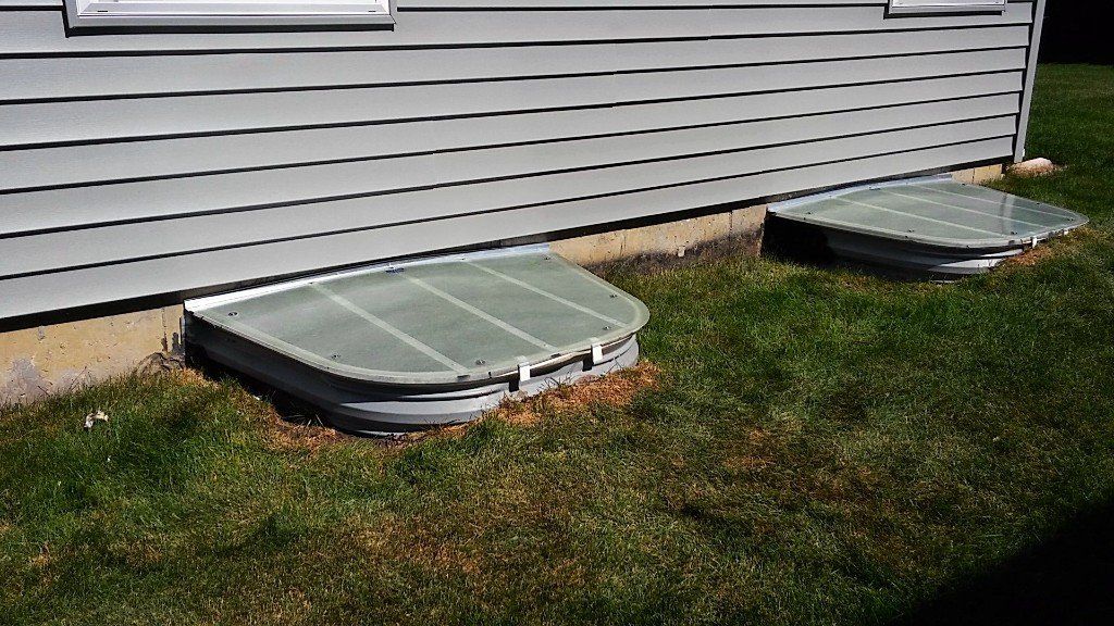 A house with two window wells in the grass