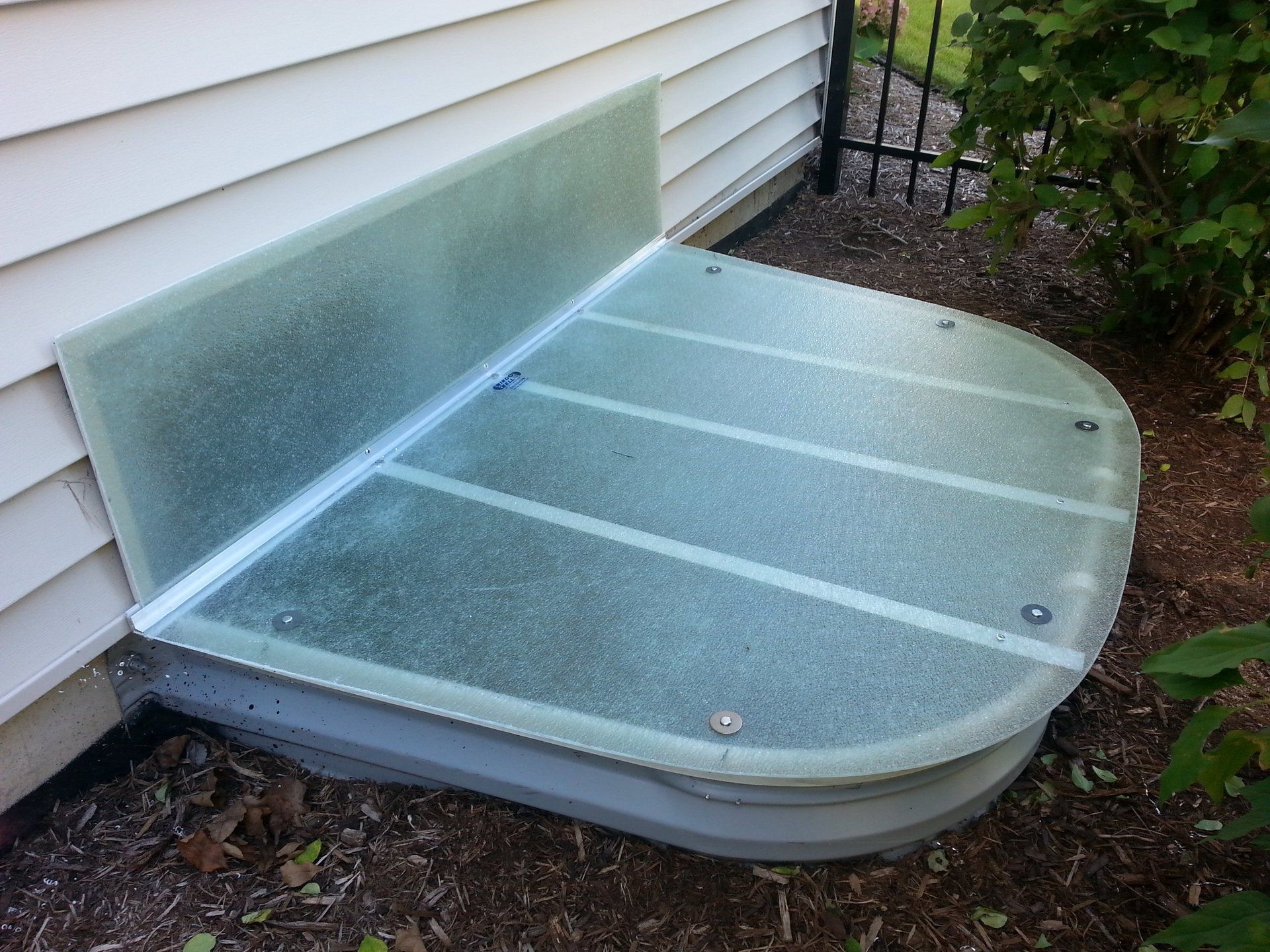 A window well with a glass cover is next to a house.