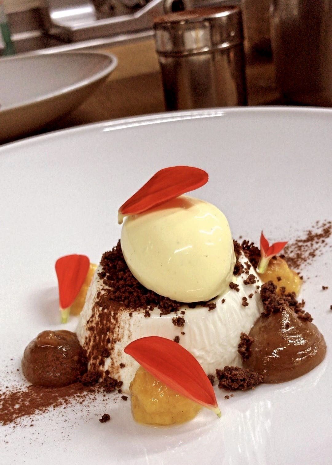 Dessert servito in una ciotola bianca, guarnito con una pallina di gelato e petali rossi.